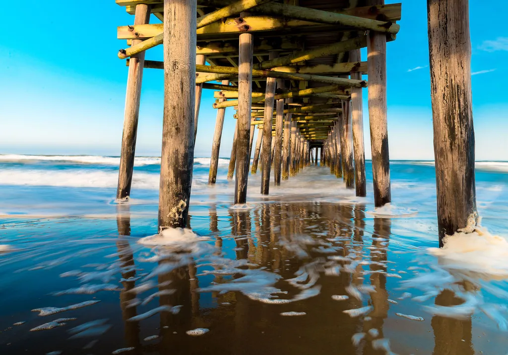 The pilings of a pier reflected in shallow blue water